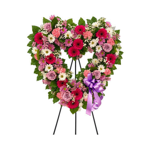 Cœur funéraire sur trépied, en roses lavande, gerberas fuchsia et marguerites, avec un ruban mauve