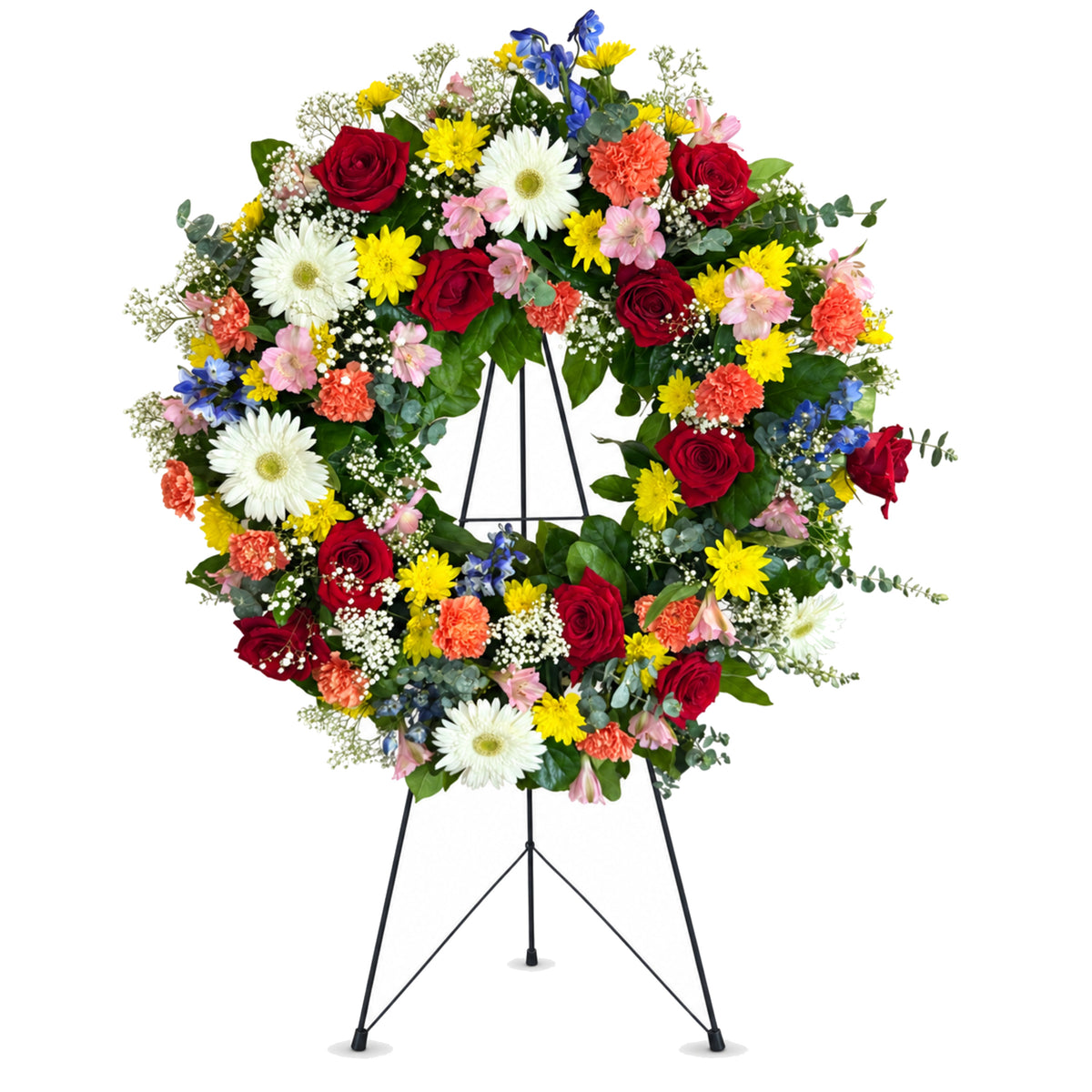 Couronne funéraire multicolore — roses rouges, gerberas blancs, chrysanthèmes jaunes, œillets orangés, alstroemerias roses et delphiniums bleus, sur trépied